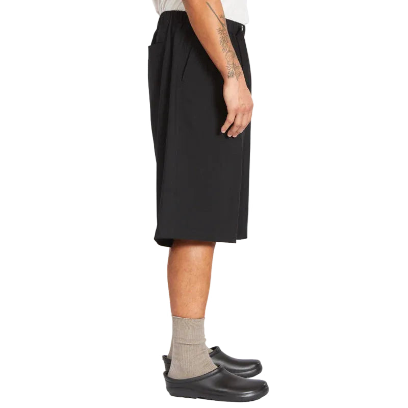 Person wearing a black shorts, gray socks, and black shoes on a white background