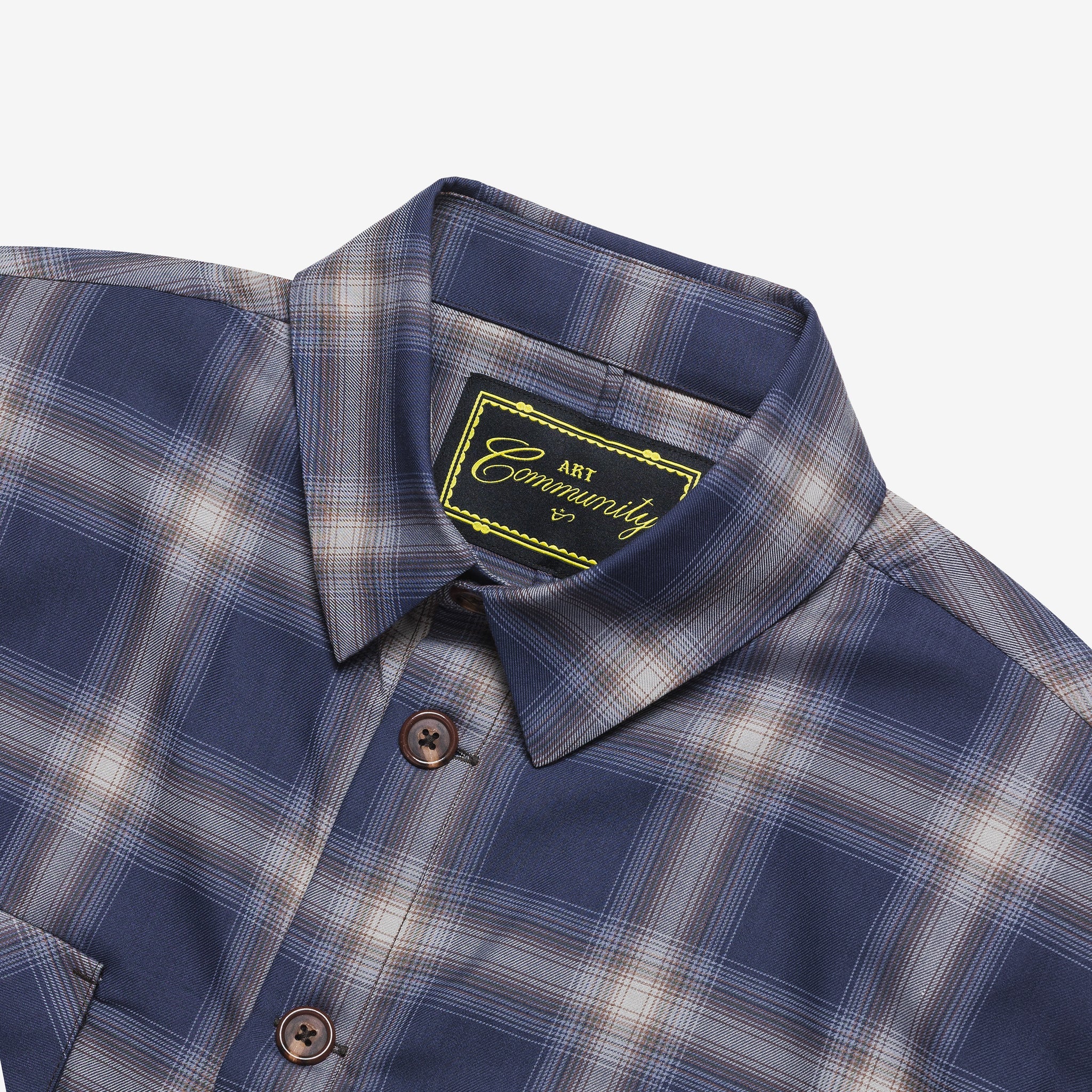 Close-up of a blue and gray plaid shirt with a brand label on a white background