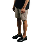 Man wearing a black t-shirt with text and beige shorts on a plain background