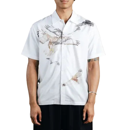 Person wearing a white shirt with bird prints, black shorts, and a black cap on a white background