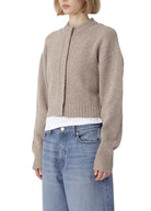 Person wearing a beige knitted cardigan and blue jeans on a white background