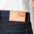 Naked & Famous denim label on a pair of jeans with a white shirt and tattooed arm in the background.