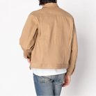 Person wearing a beige jacket and blue jeans on a white background