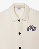 Beige shirt with black embroidered design and button details on a white background