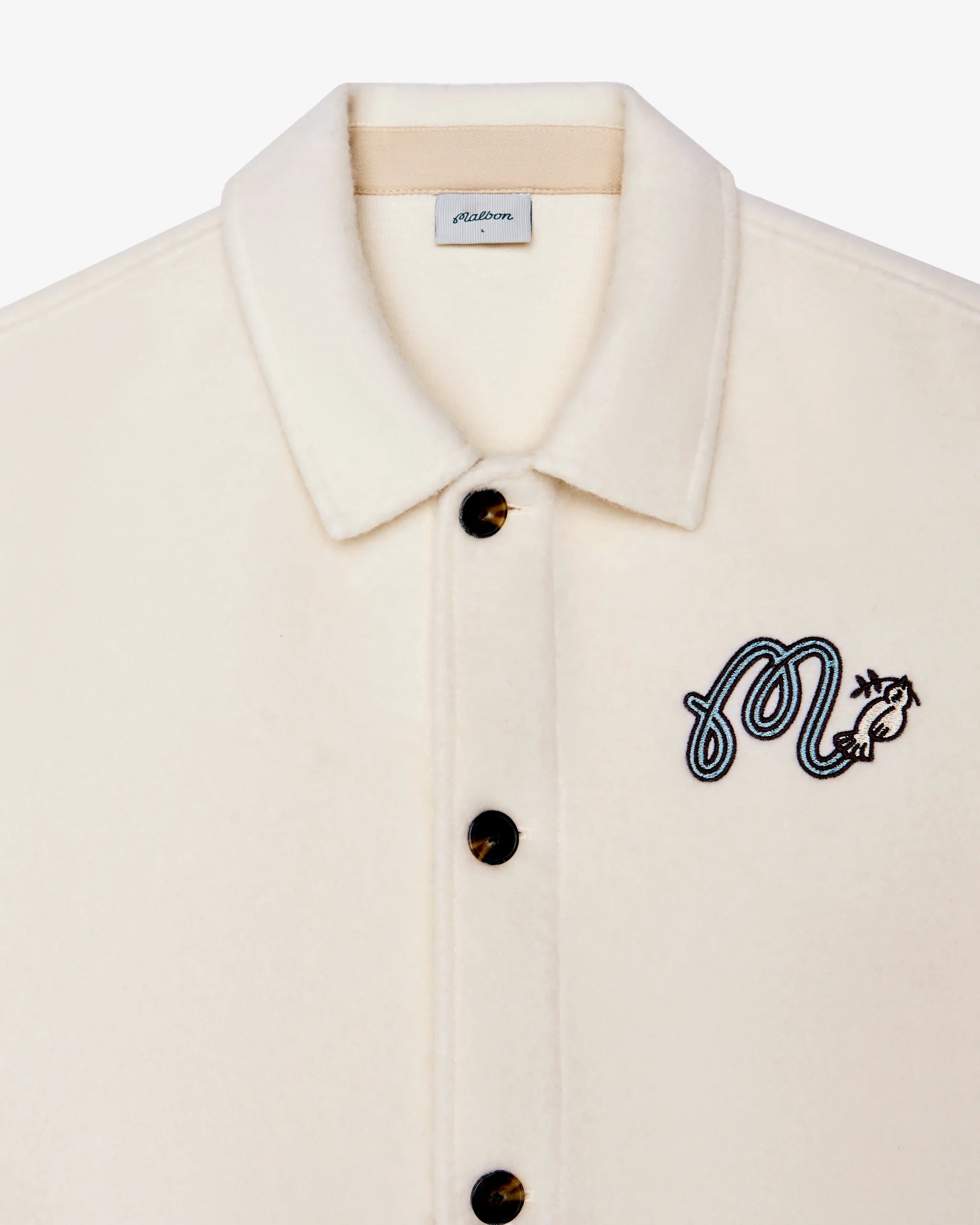 Beige shirt with black embroidered design and button details on a white background