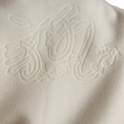Person wearing a white jacket with an embossed design on the back against a brown background