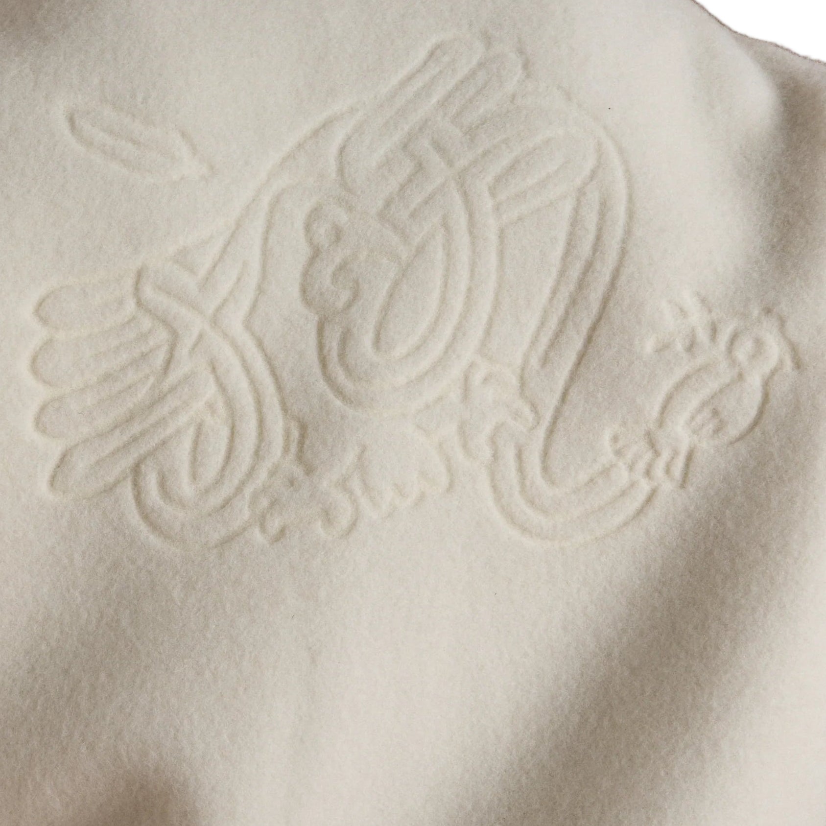 Person wearing a white jacket with an embossed design on the back against a brown background