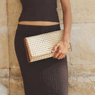 Woman holding a woven clutch against a stone wall