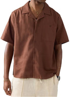 Man wearing a brown shirt and beige cap with a logo on a white background