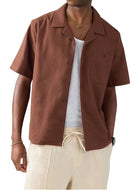 Man wearing a brown short-sleeve shirt and beige pants on a light gray background