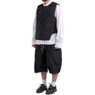Person wearing a black vest over a white shirt with black shorts on a white background