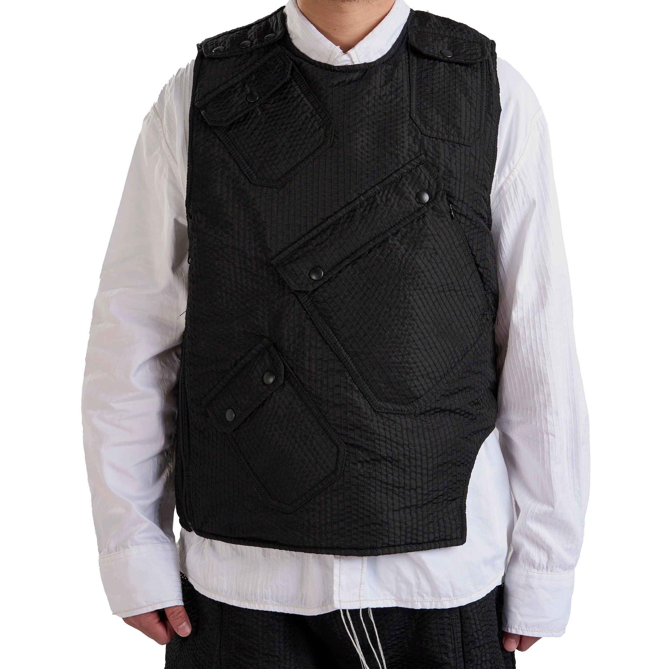 Person wearing a black quilted vest over a white shirt on a white background