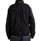 Black fleece vest with purple skeleton design on the back, worn by a person.