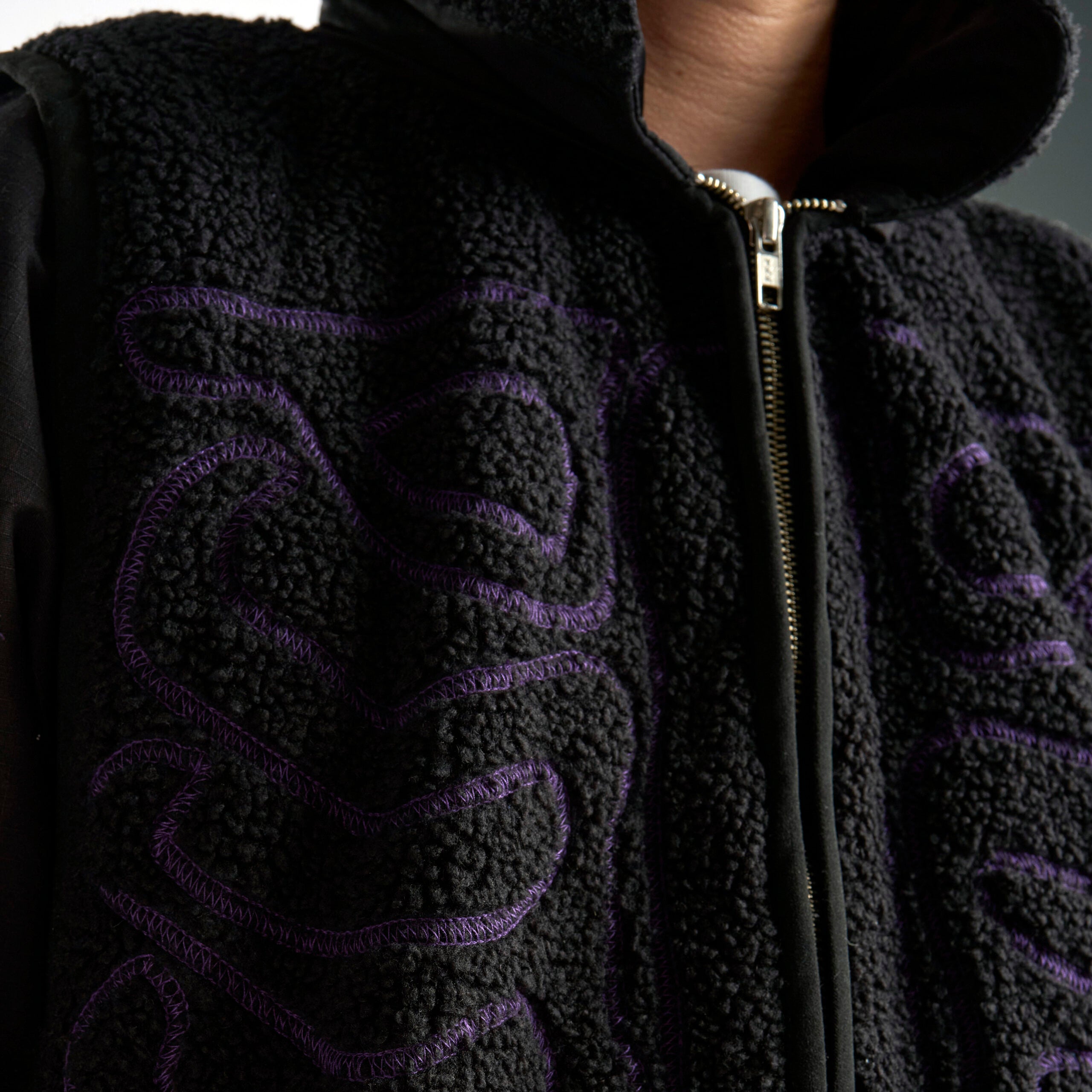 Black fleece jacket with purple embroidery on a neutral background