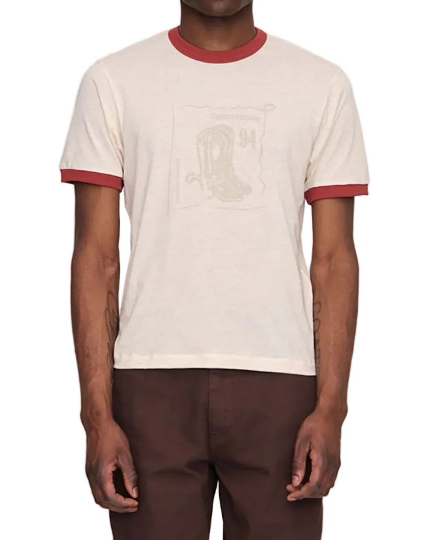 Man wearing a cream t-shirt with red trim and brown pants on a white background