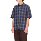 Person wearing a blue plaid shirt and brown pants on a white background
