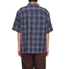 Person wearing a blue plaid shirt and brown pants on a white background. Back view