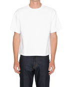 Person wearing a plain white t-shirt and dark jeans on a light gray background