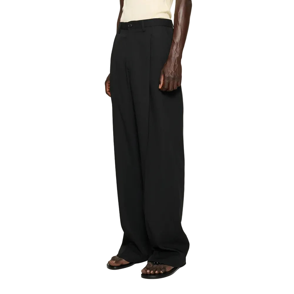 Person wearing a beige tank top and black wide-leg pants with a black knit hat on a white background