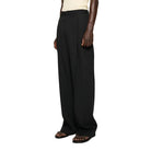 Person wearing a beige tank top and black wide-leg pants with a black knit hat on a white background
