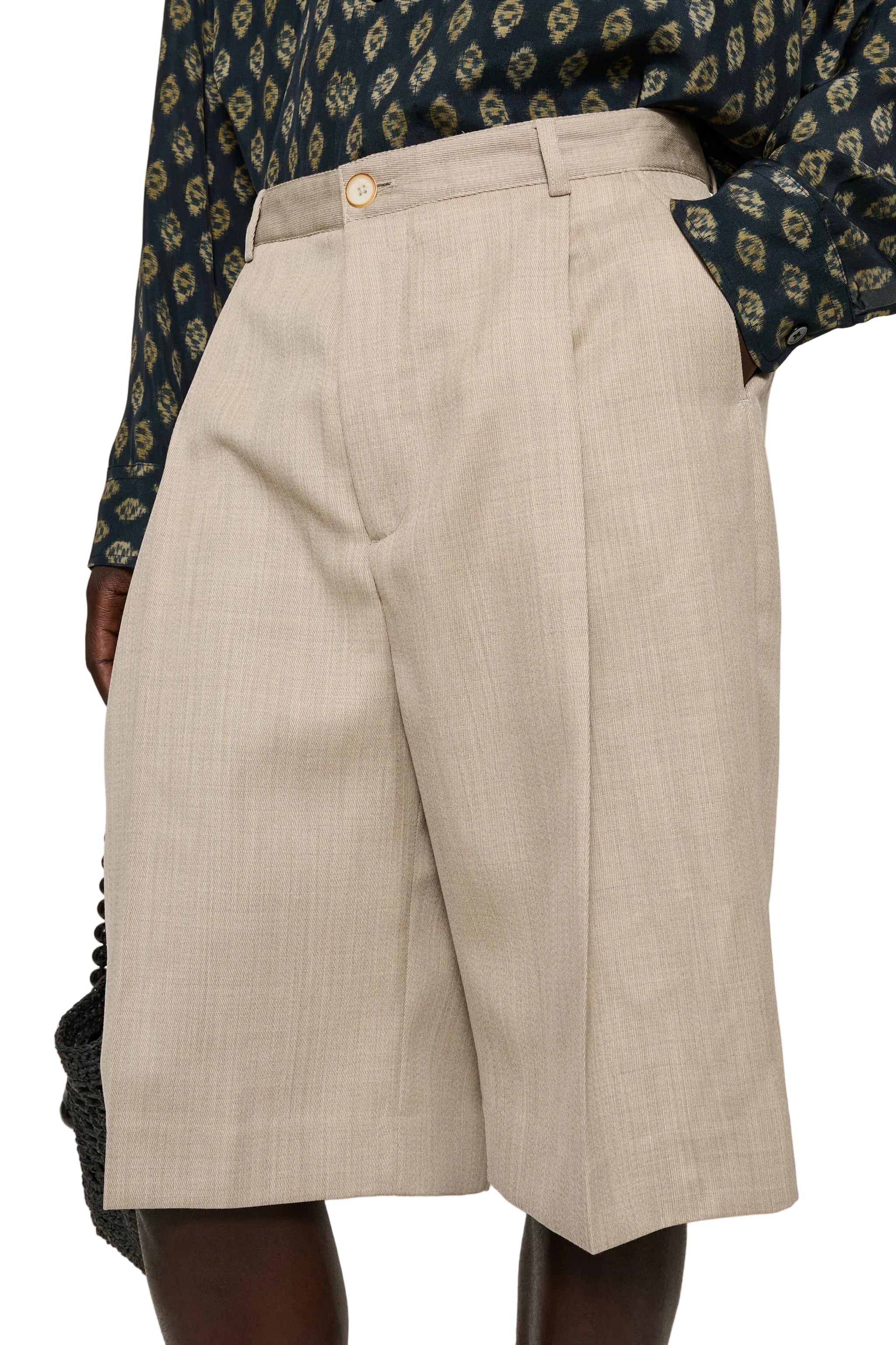 Beige shorts worn by a person with a patterned top on a white background