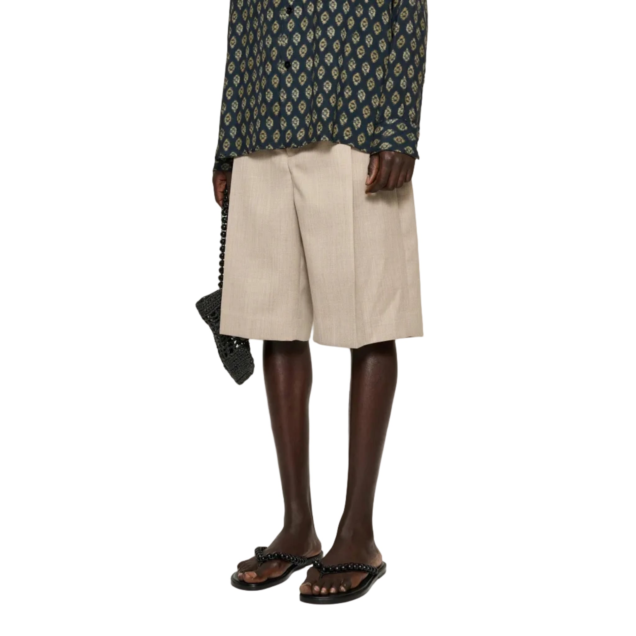 Man wearing a patterned shirt and beige shorts on a white background
