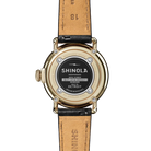 Back of a Shinola watch with a gold case and tan leather strap on a white background
