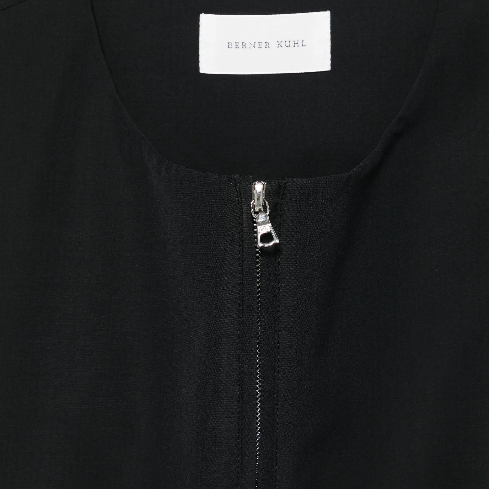 Close-up of a black garment with a zipper and 'BERNER KUHL' label.