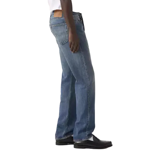 Person wearing a white t-shirt and blue jeans standing against a plain background