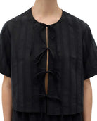 A close-up of a model wearing a black short-sleeve cropped top with vertical textured stripes and a front tie closure.