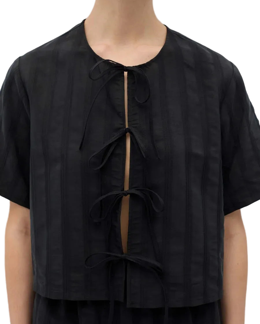 A close-up of a model wearing a black short-sleeve cropped top with vertical textured stripes and a front tie closure.