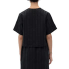 Back view of a model wearing a black short-sleeve cropped top with vertical textured stripes.