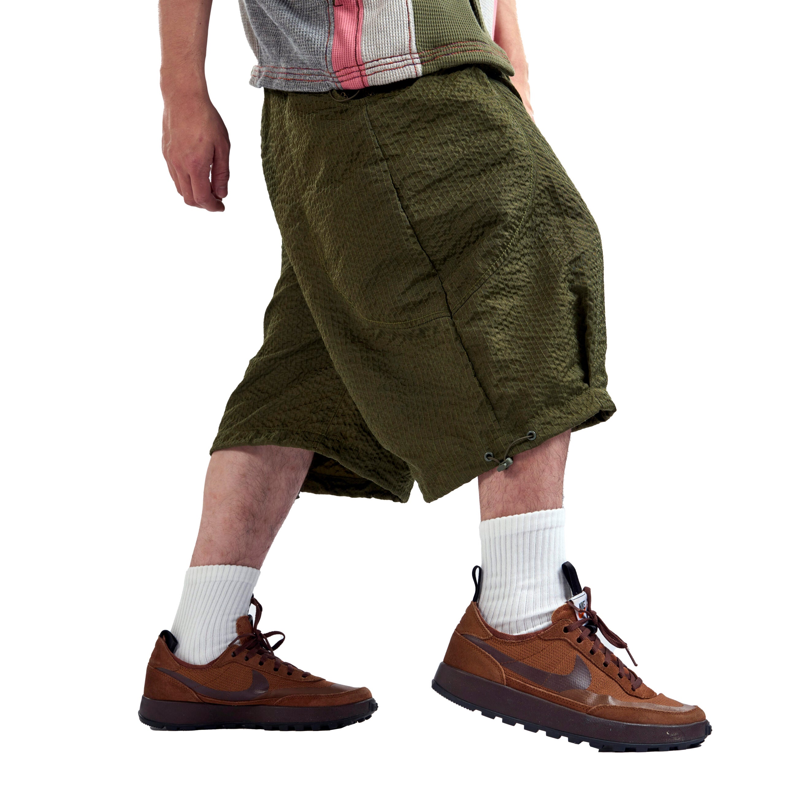Person wearing green baggy shorts and brown shoes on a white background