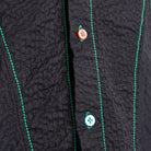 Close-up of a textured black garment with green stitching and buttons.