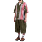 Person wearing a colorful patchwork shirt and green pants on a white background