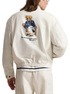 Person wearing a white jacket with a Polo Bear Ralph Lauren logo on the back.