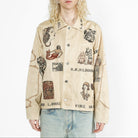 A model with long blonde hair wearing a beige button-up shirt jacket covered in vintage-style illustrated patches and text, paired with light blue jeans, against a plain white background.
