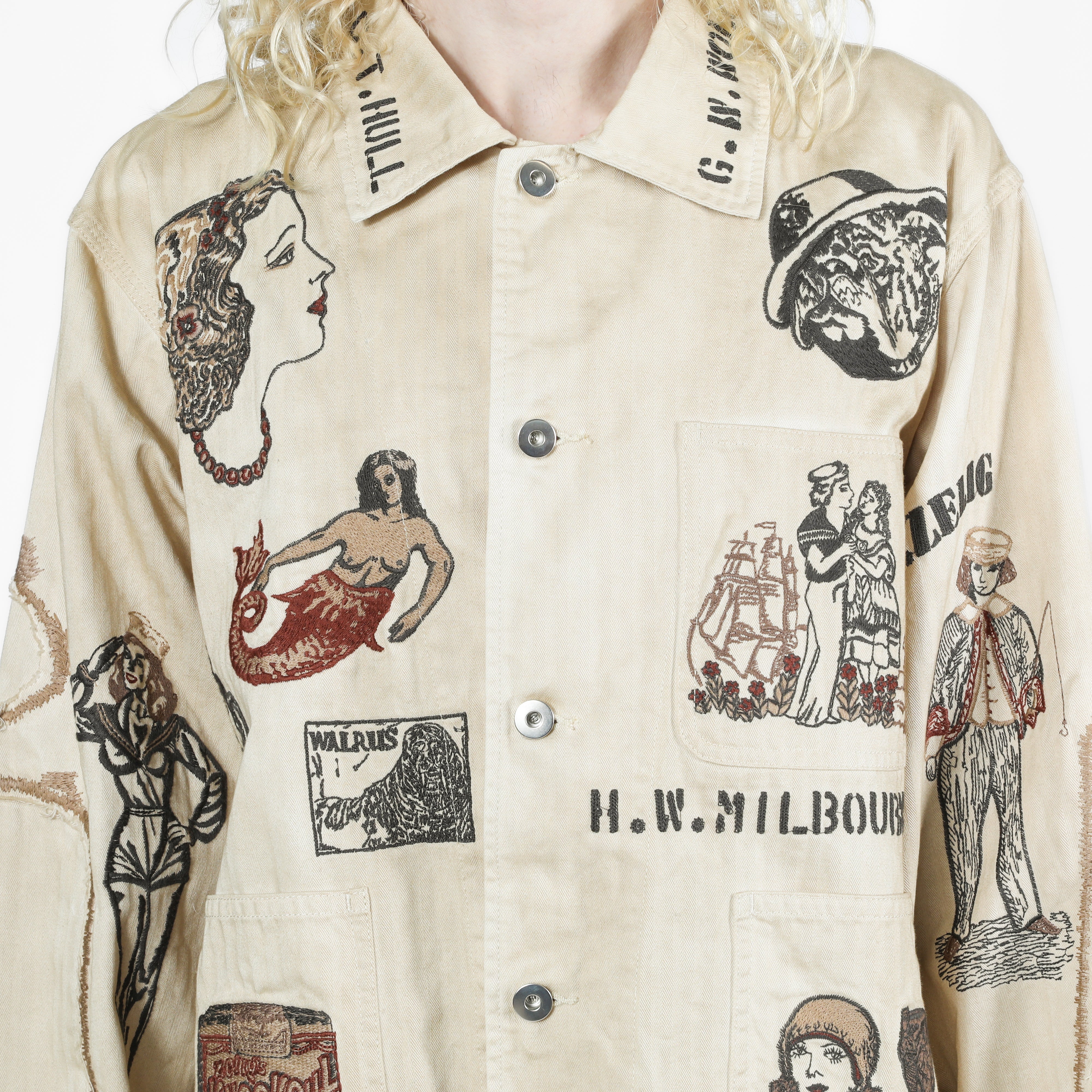 A close-up of a cream-colored button-up shirt with vintage-style illustrated graphics and text prints, worn by a model.