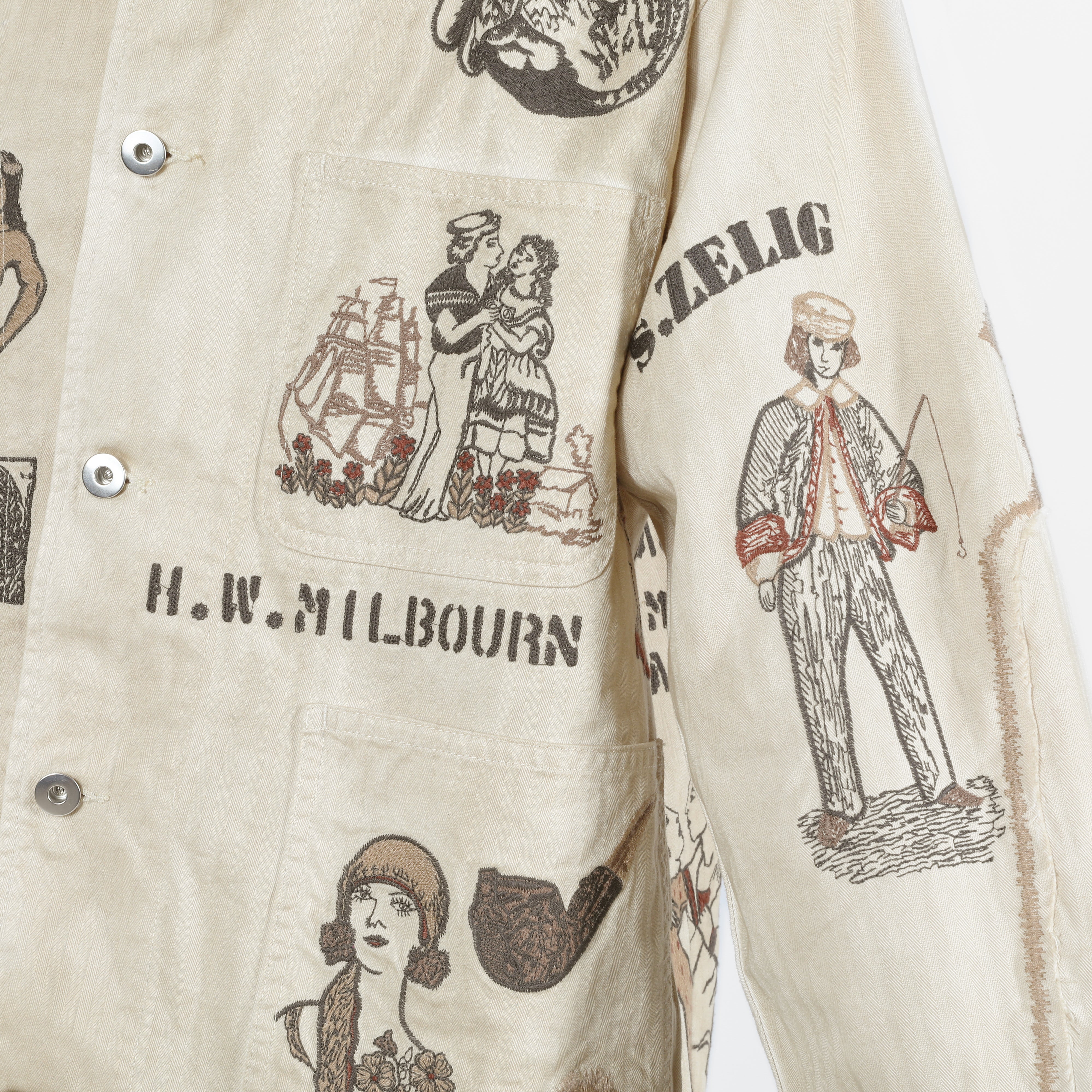 Close-up of a cream-colored button-up shirt featuring vintage-style illustrated prints and text including 'H.W. MILBOURN'