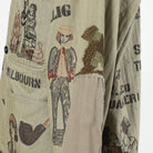 Close-up of a beige canvas jacket with a vintage-style illustrated print featuring figures, a smoking pipe, and text including 'MILBOURN'.