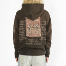 A person shown from the back wearing a dark brown hoodie with a large vintage-style graphic print on the back. The hoodie has distressed detailing and text elements in muted red, beige, and white.
