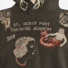 Close-up of a dark brown hoodie featuring embroidered graphics and text reading 'ST. DENIS PORT TRAINING ACADEMY' with '502' and decorative figures.