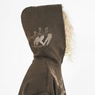 A close-up side view of a person wearing a dark brown hooded sweatshirt with a light beige graphic print of three figures on the hood, against a plain white background.