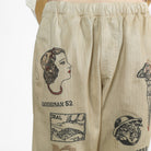 Beige herringbone pants featuring vintage-style embroidered illustrations and text including 'GOODMAN 52' and 'SEAL'.