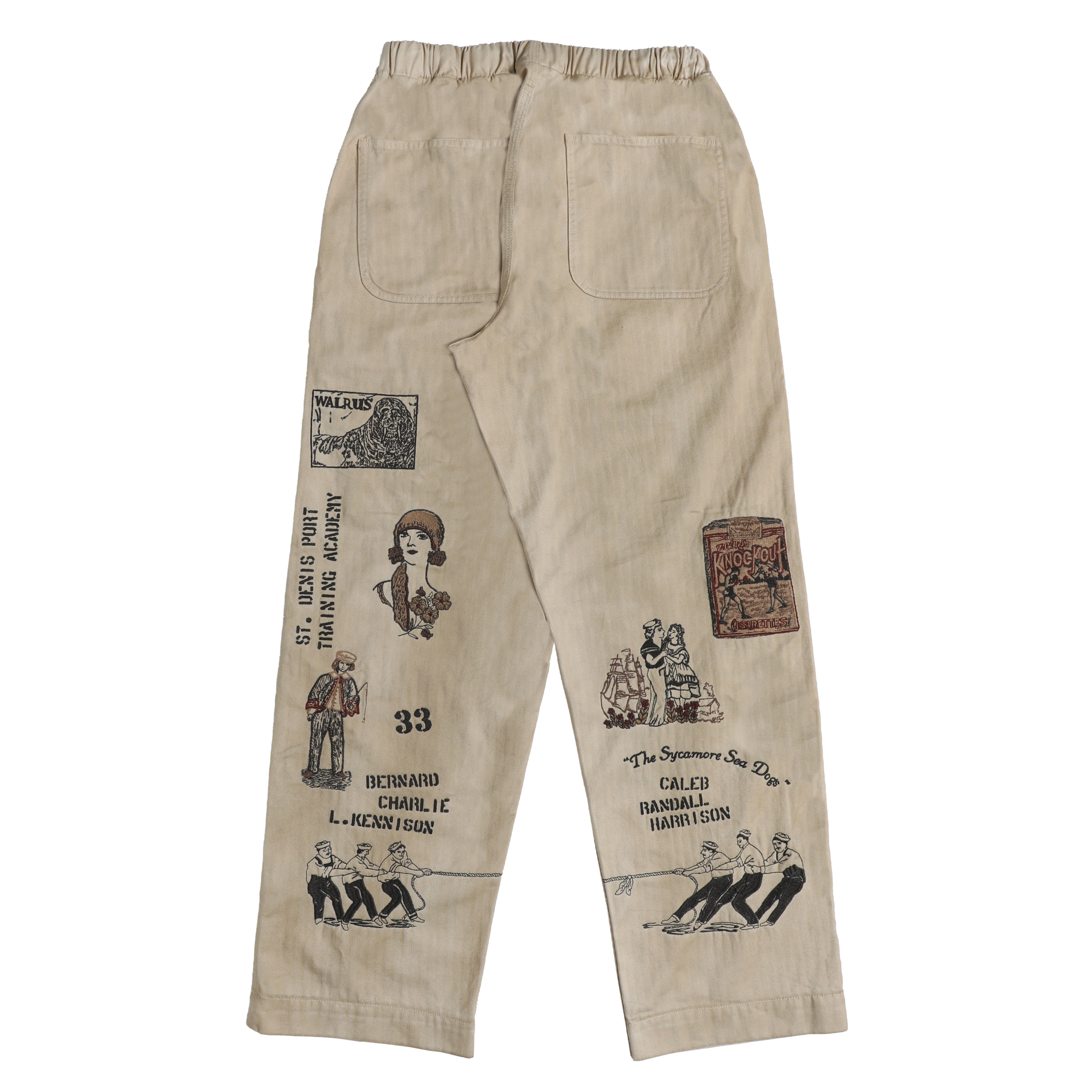 Beige pants with black embroidered vintage-style illustrations and text on both legs, featuring an elastic waistband and back pockets.