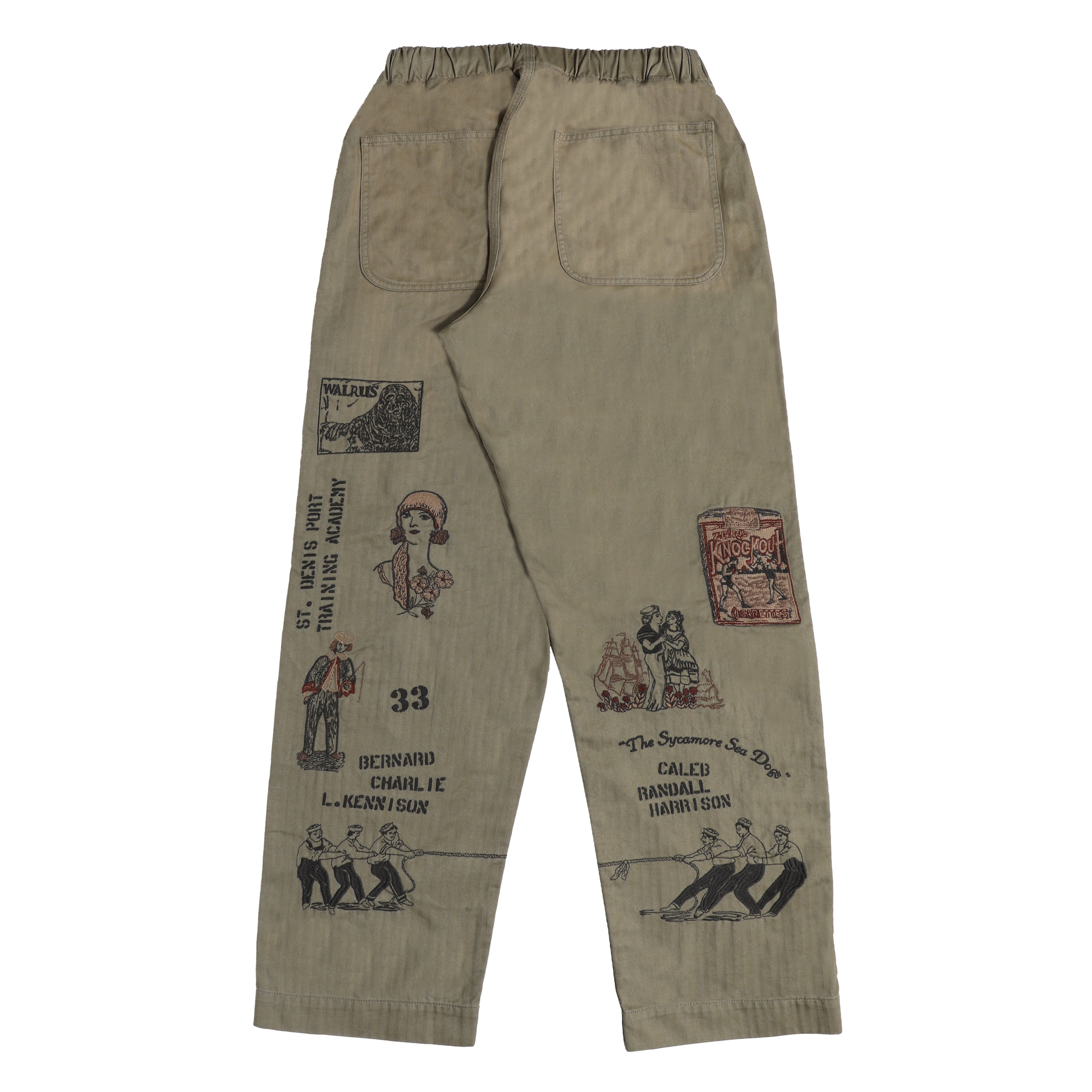 A pair of beige cargo pants shown from the back, featuring a drawstring waist, two back patch pockets, and multiple black and red embroidered graphics depicting vintage-inspired figures and text.