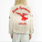A model viewed from behind wearing a heavily distressed cream-colored jacket with a large red graphic on the back reading 'North Sycamore GAS & OIL' and featuring a winged figure. The model is also wearing light-wash jeans against a plain white background.
