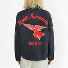 A person viewed from the back wearing a faded black jacket with a large red and white North Sycamote Gas & Oil winged logo graphic on the back, paired with light gray jeans against a white studio background.