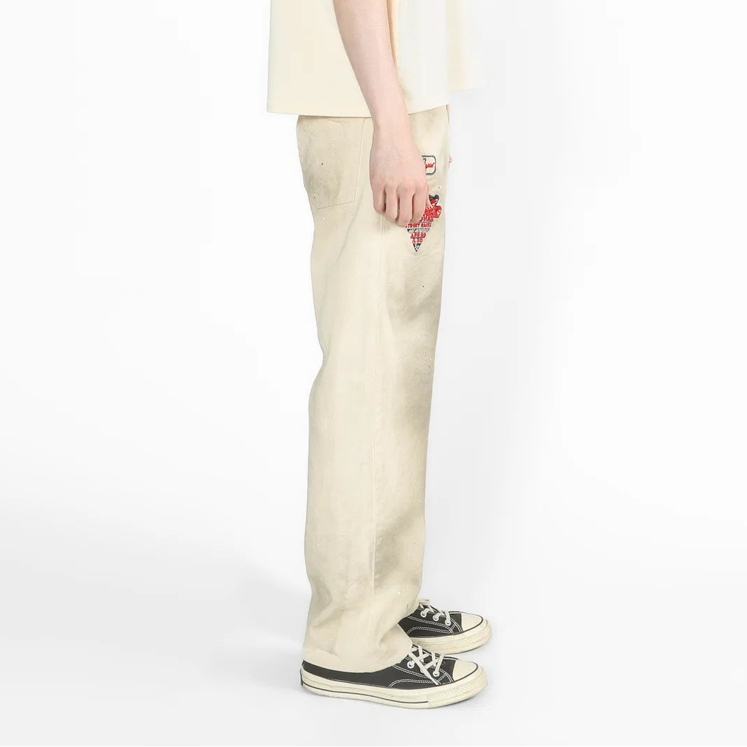 A model shown from the side profile wearing a cream-colored oversized short-sleeve t-shirt and matching cream wide-leg trousers, paired with black and white canvas sneakers, against a plain white studio background.