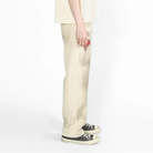 A model shown from the side profile wearing a cream-colored oversized short-sleeve t-shirt and matching cream wide-leg trousers, paired with black and white canvas sneakers, against a plain white studio background.